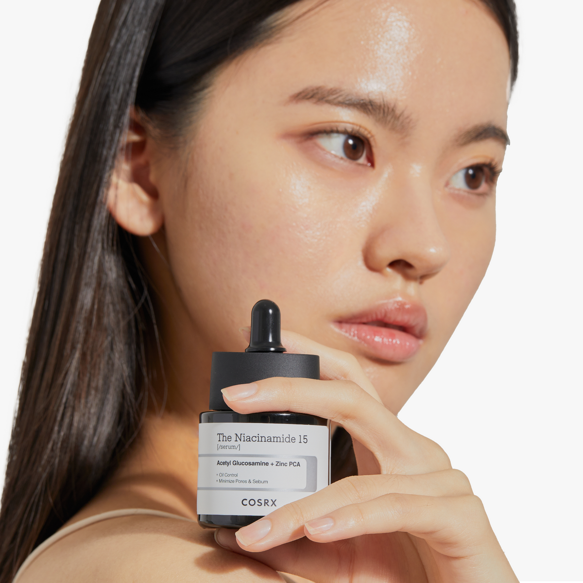 Model holding COSRX The Niacinamide 15 Serum near her face, showcasing a hydrated, radiant complexion. The 15% niacinamide formula is clinically tested for acne-prone and oily skin, reducing oiliness, dark spots, and rough texture while supporting barrier health. Clinical trials showed a 42.72% decrease in blackheads and a 50% reduction in whiteheads after 4 weeks of use.