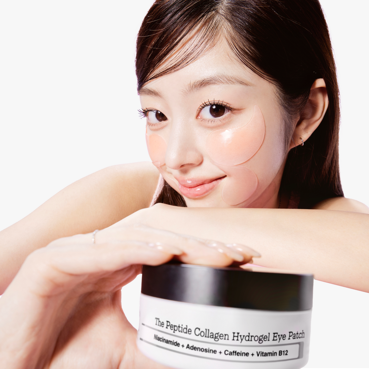 Model with COSRX The Peptide Collagen Hydrogel Eye Patch applied under eyes, smiling while holding the jar; pink hydrogel pads visibly adhere to skin, formulated with collagen and peptides to lift, firm, and brighten the under-eye area for youthful radiance.